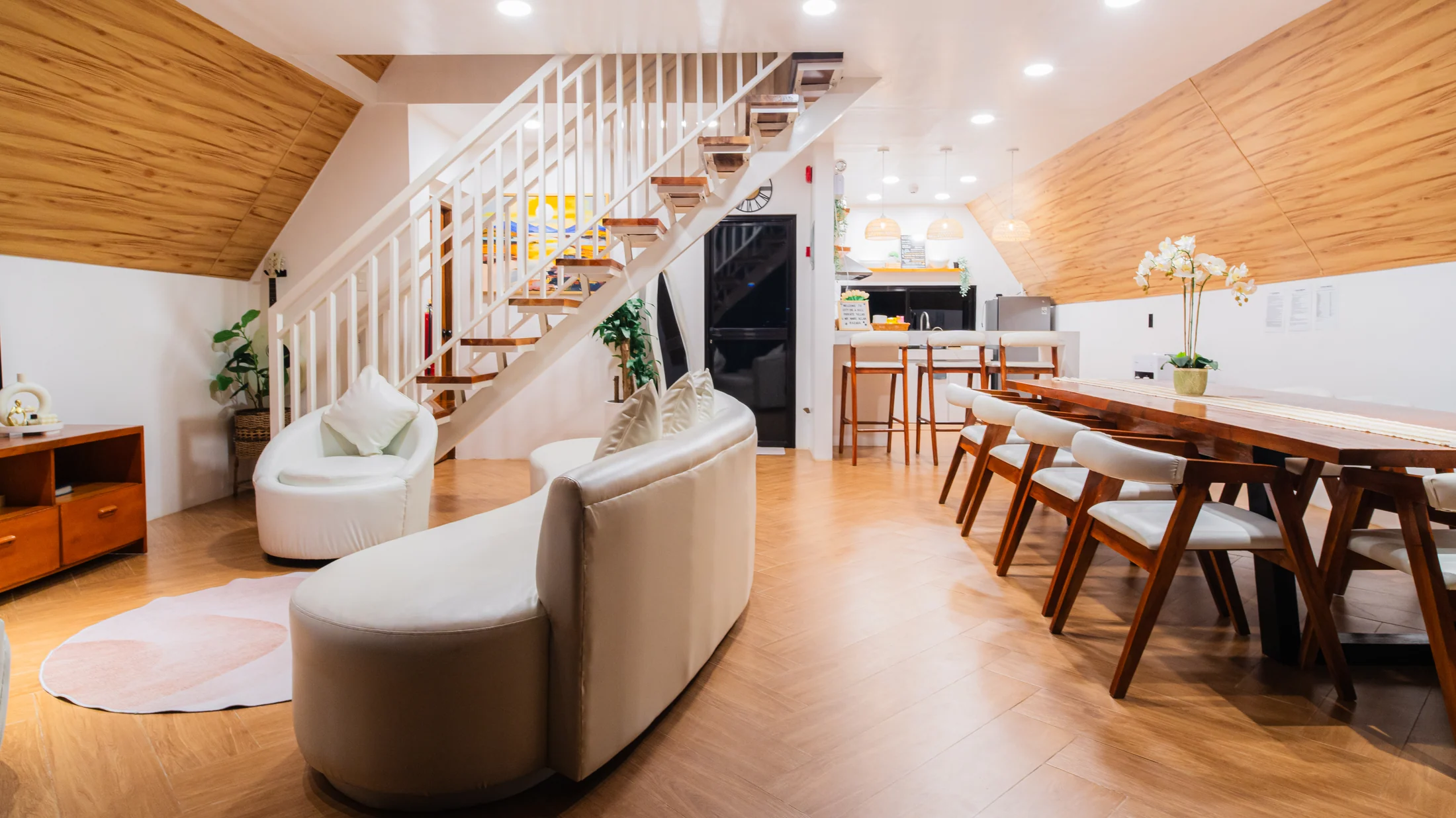 Open living and dining space beneath a timber ceiling and white staircase at City on a Hill