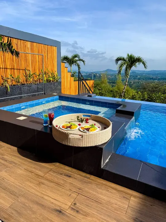 A tray of fruit and drinks on the jacuzzi ledge beside the spillover into the pool.