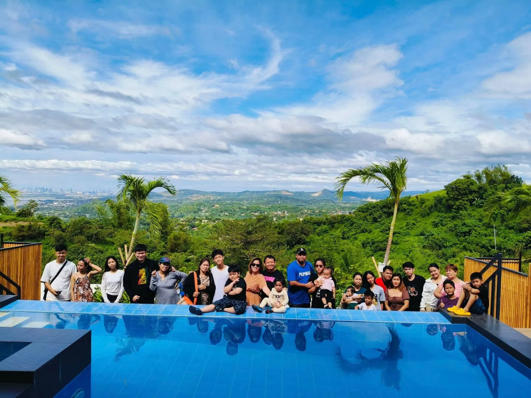 Guests gathered at the edge of a private infinity pool, green hills and the city skyline behind.