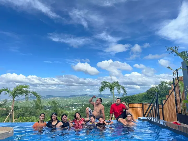 Guests in the infinity pool under a wide blue sky, palms and hills beyond.