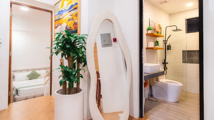 A hallway with a sculpted mirror, opening onto a bathroom with a rain shower.