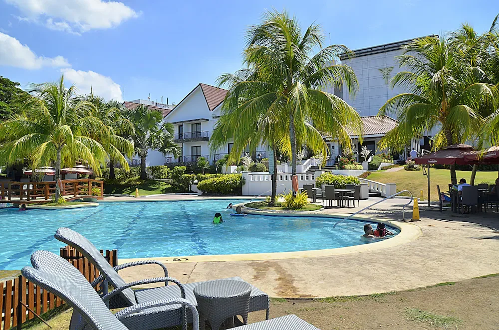 A resort pool with palm trees, loungers and a hotel building behind