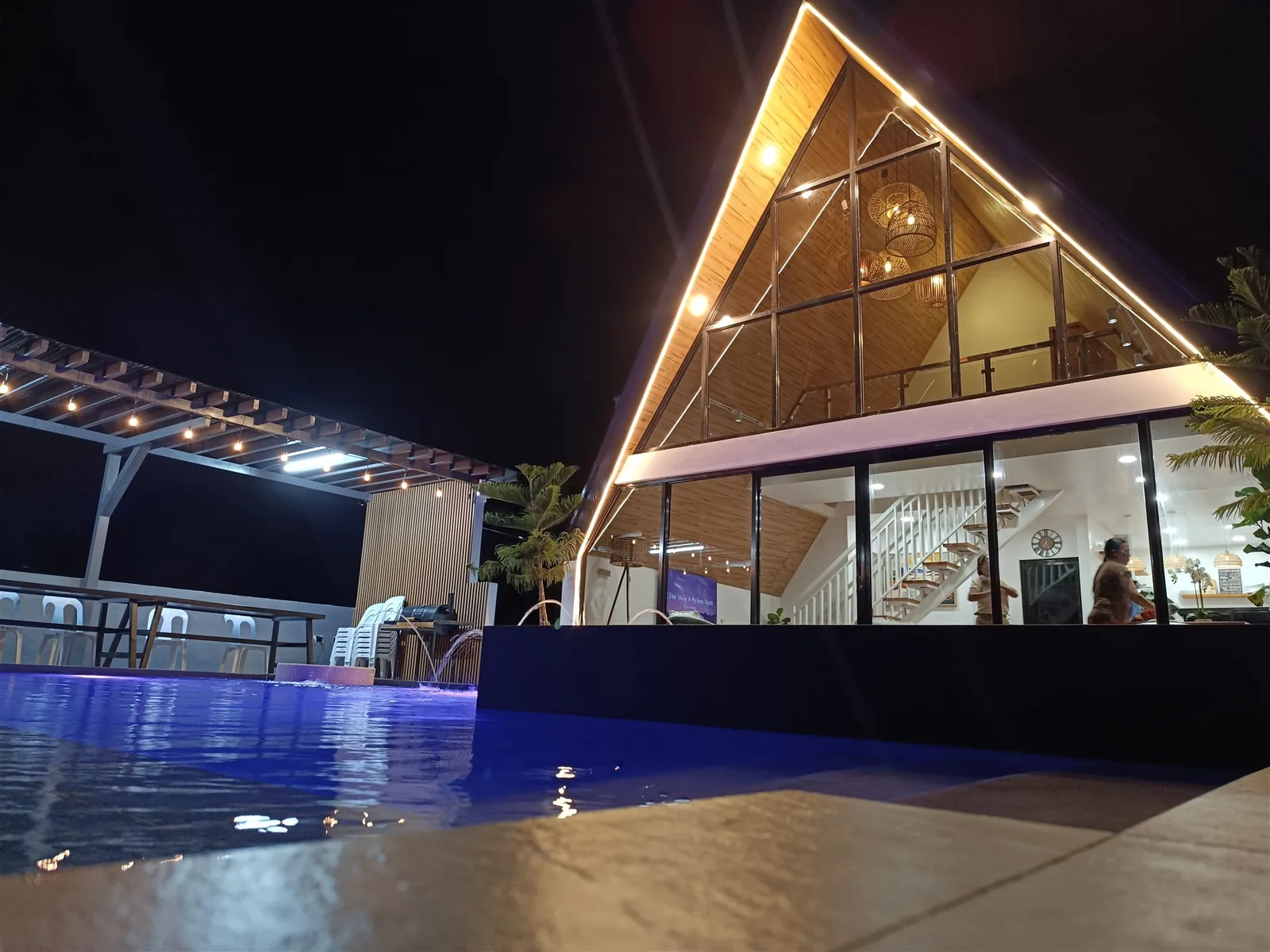 A-frame villa with lit glass facade and pool at night