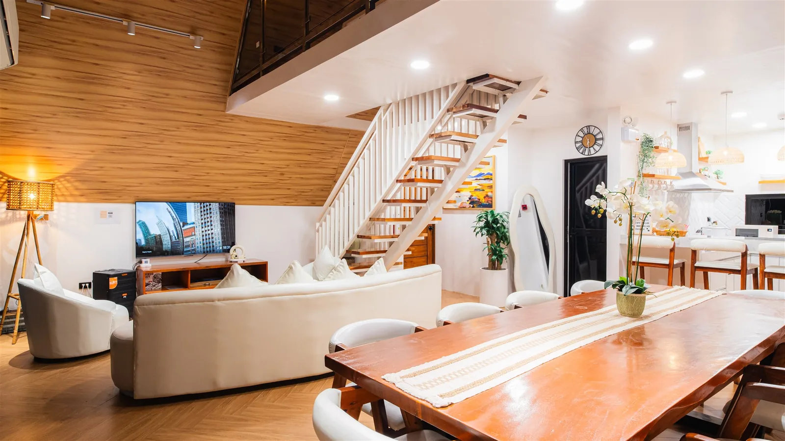 Double-height villa living room with white sofas, a wooden staircase and tall windows