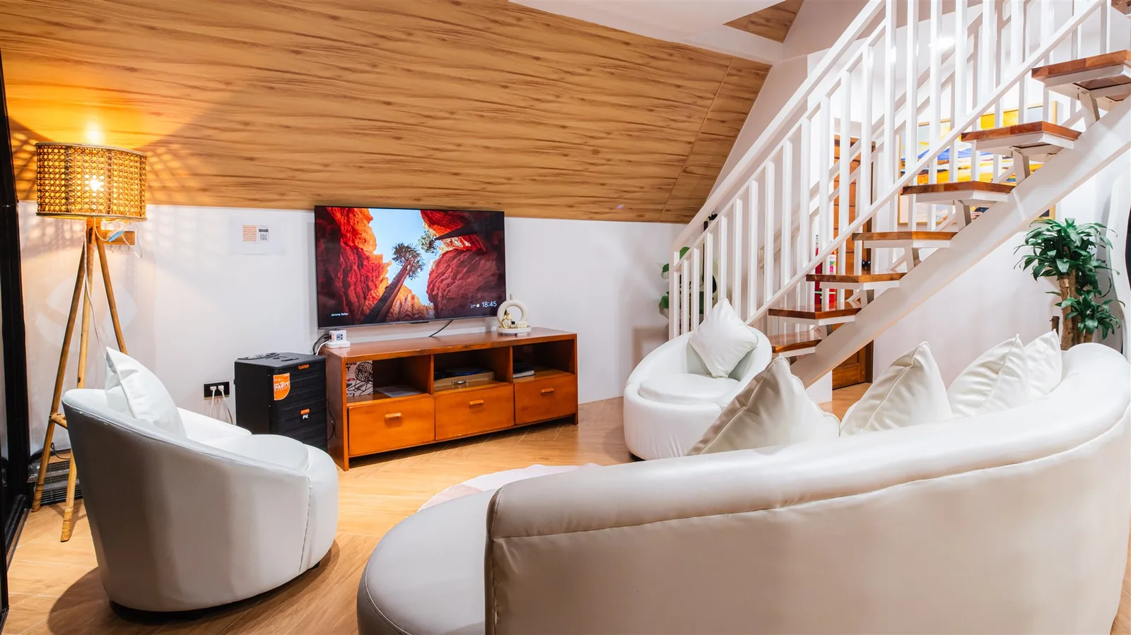 Villa living room with curved white sofas, a TV area and a wooden staircase