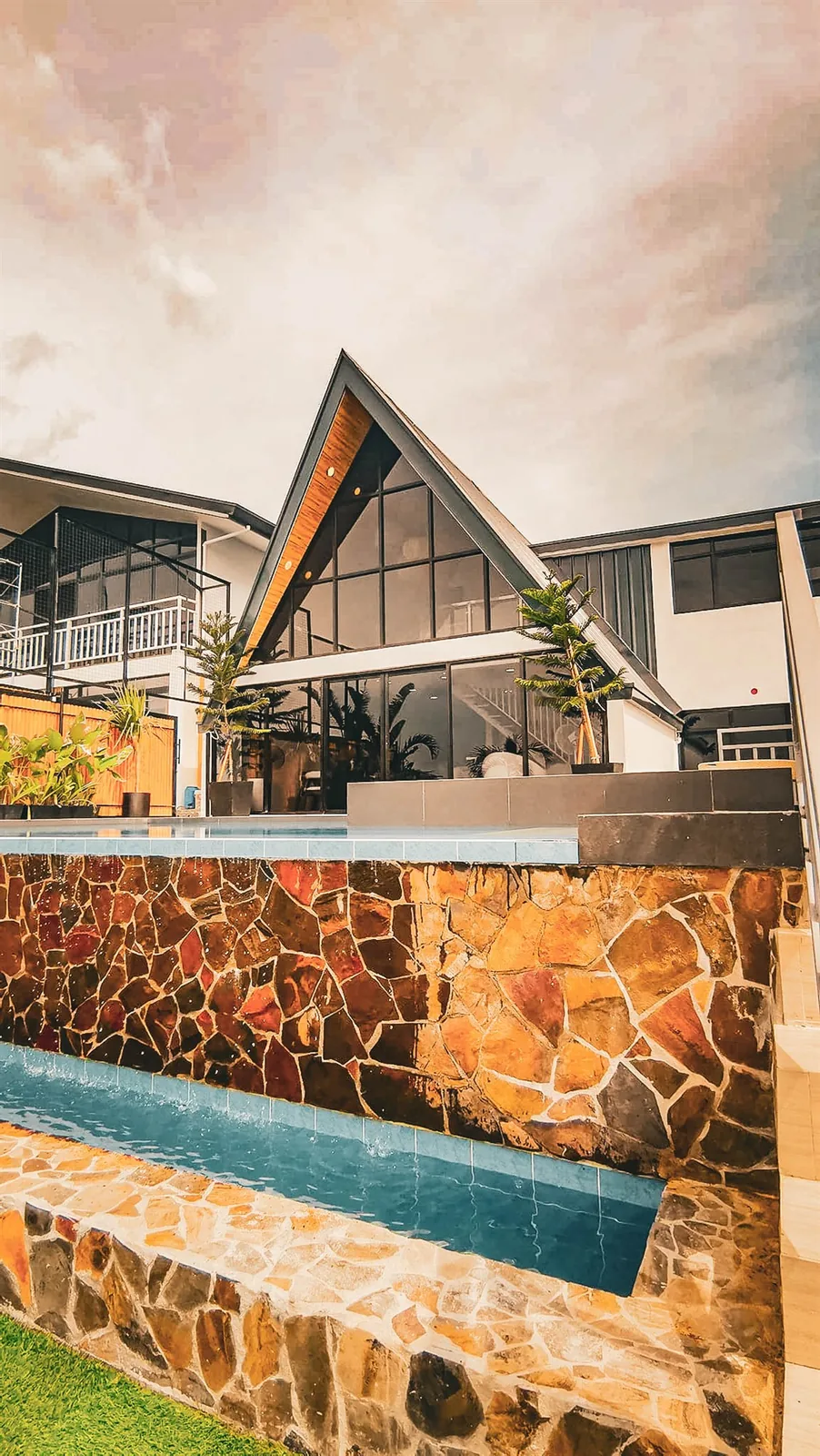 Zuriel villa, an A-frame with dark glass and a stone-clad pool edge, on the hillside in Binangonan