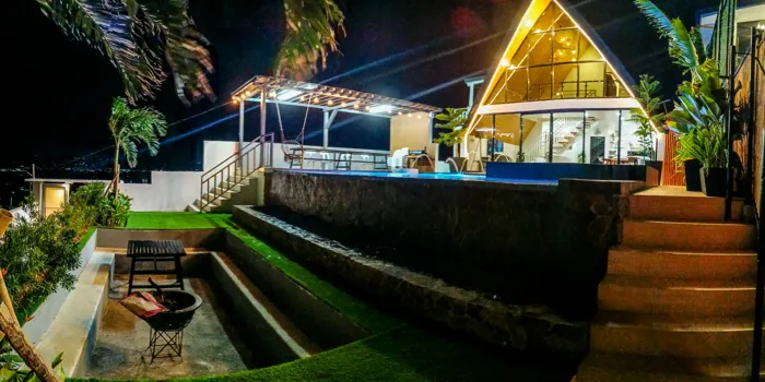 Zachary at night, lit from within, with a fire bowl and lounge area below the facade.
