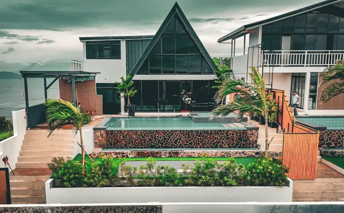 Zachary: an A-frame villa with a glass front, its pool and stone wall in the foreground.