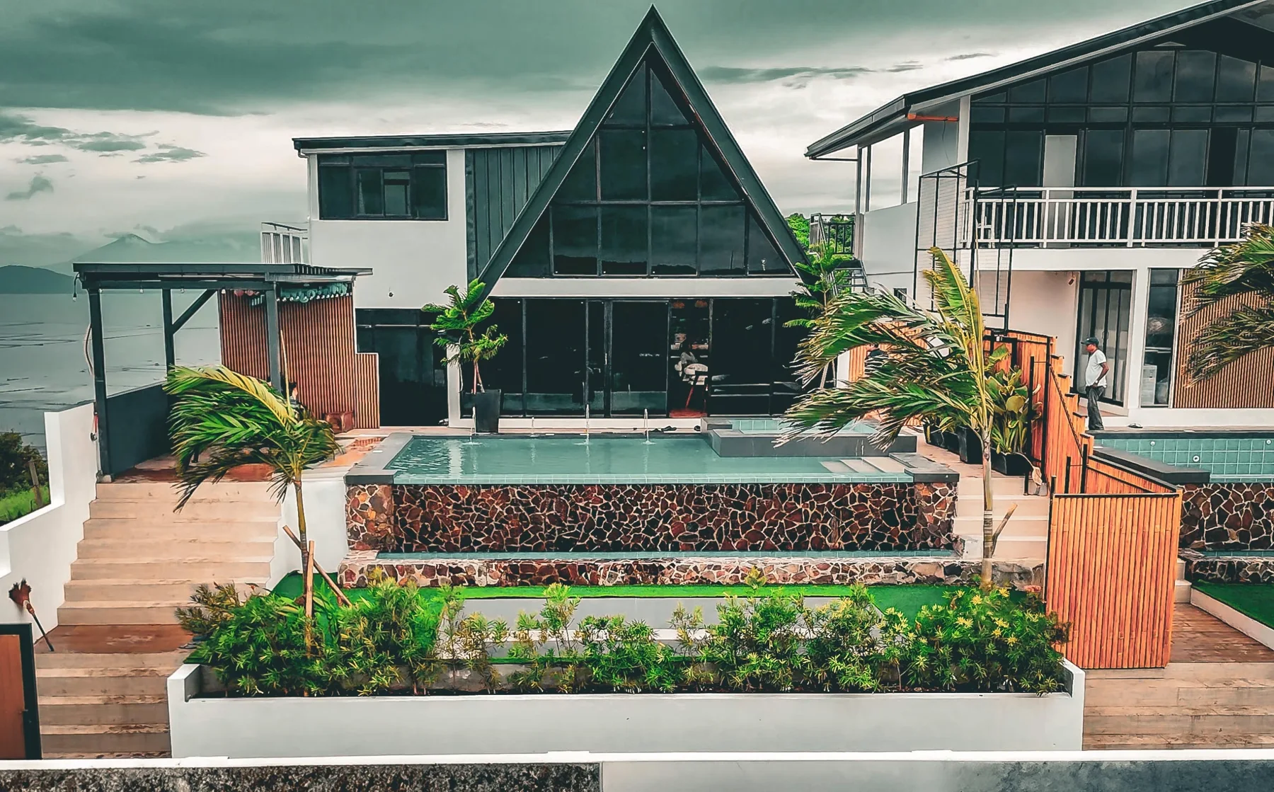 Zachary: an A-frame villa with a glass front, its pool and stone wall in the foreground and the lake on the left.