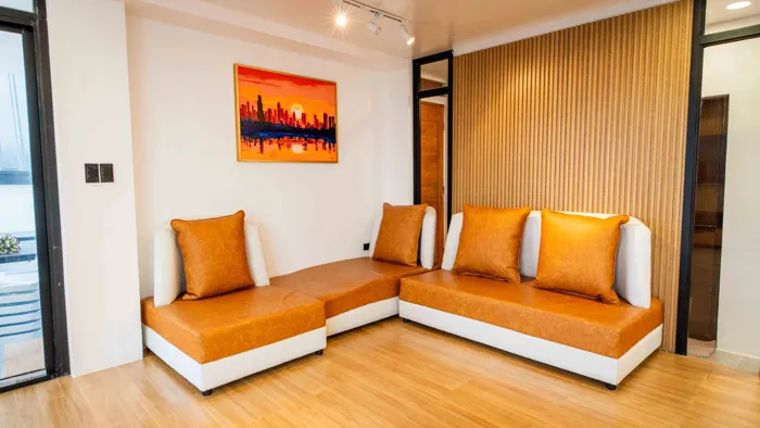 A living area in Zoie with an orange corner sofa and a timber-slatted wall.